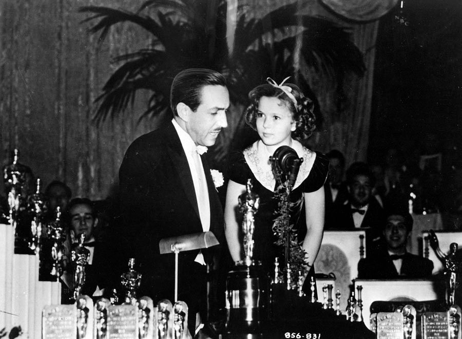 Nine–year–old Shirley Temple presents to Walt Disney a special Oscar for “Snow White and the Seven Dwarfs” recognized as a significant screen innovation which has pioneered a great new entertainment field for the motion picture cartoon. Event was the 1938 Academy Awards. — Photo: Walt Disney Productions.