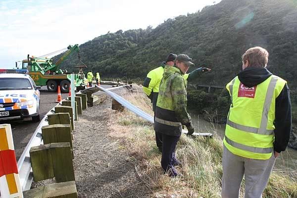 Emergency workers stand next to the barrier where a car crashed through before plunging 20 metres in to the Manawatu River. — FAITH SUTHERLAND/Manawatu Standard.
