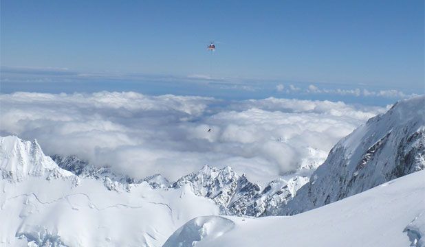 A rescue helicopter recovers the dead climber from the lower summit of Aoraki-Mount Cook with the aid of Department of Conservation Aoraki-Mt Cook Alpine Rescue Team leader Karen Jackson. The man fell over the back of the saddle (beneath the helicopter) while skiing at 3700 metres. — Photo: Brent Swanson.