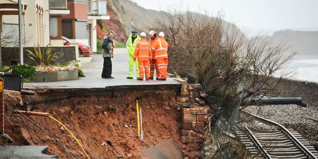 Workmen assess a huge hole exposing ground services and exposed railway track after the sea wall collapsed in Dawlish, England.  Photo: Associated Press.