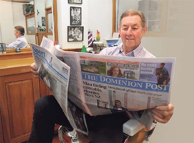 Retailer John Grant reads The Dominion Post while seated in one of his barber's chairs.