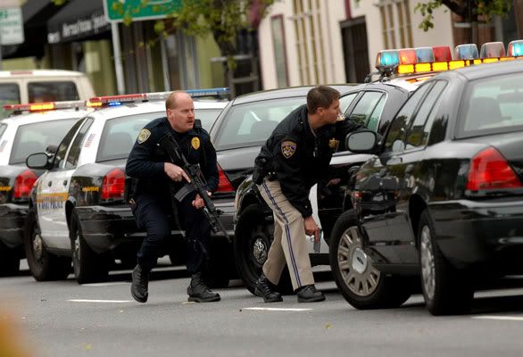 Law enforcement officers find cover behind a car in Oakland while responding to the day's second shooting in which officers were shot. (Dan Rosenstrauch/Bay Area News Group)