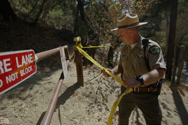 Senior Park Ranger Flint Glines uses tape to block off a hiking trail closed during the search for a mountain lion that attacked a 6-year-old boy on Sunday. — Photo: Jessica Christian/San Francisco Chronicle.