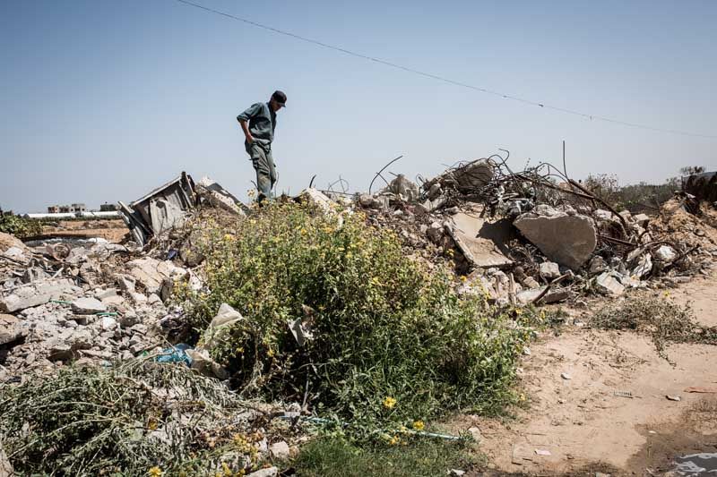 A man living in the Shuka neighborhood walks across the rubble of a destroyed house.