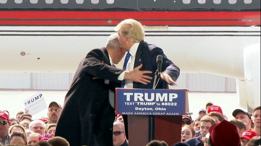 In this image from the television network pool, a Secret Service agent rushes onto the stage to protect Republican presidential candidate Donald Trump after a man attempted to get beyond the barricades to the dais where Trump was standing during a speech at Dayton International Airport in Vandalia, Ohio. — Photograph: TV network pool via Associated Press.